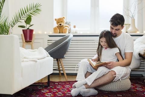 Padre e hija leyendo junto al radiador de su salón