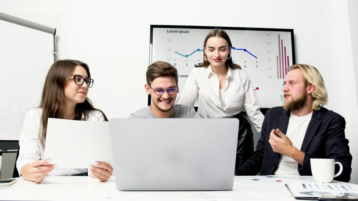 grupo de dos hombres y dos mujeres consultando un ordenador port&aacute;til con una expresi&oacute;n de satisfacci&oacute;n en el rostro.